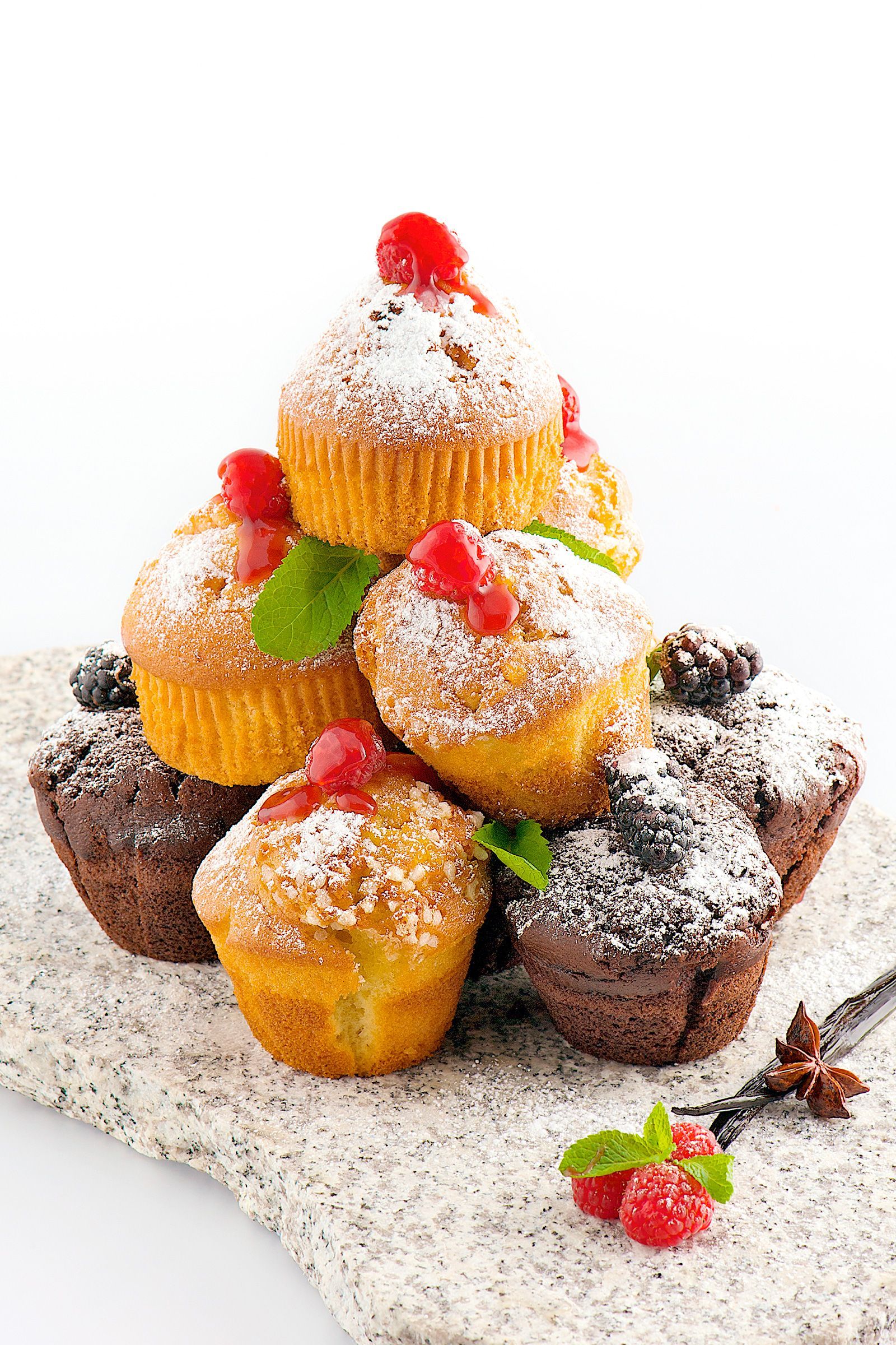 A pyramid of muffins, yellow and chocolate, dusted with powdered sugar, topped with cherries and berries.