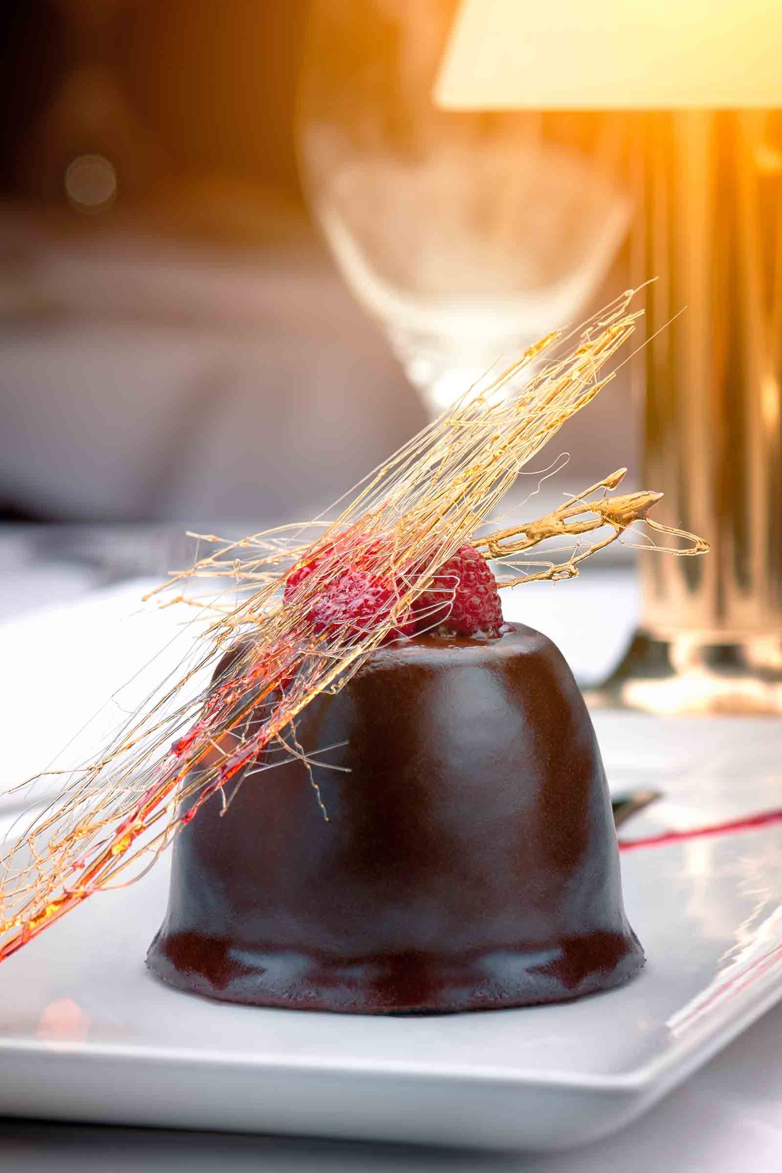 Dark chocolate dessert with raspberry and spun sugar garnish.