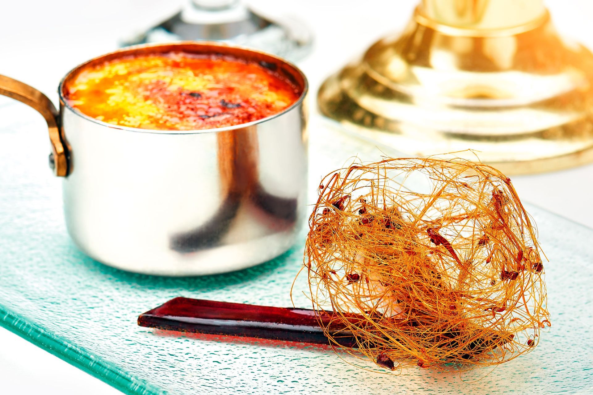 Dessert: A ramekin of baked custard, a spun sugar nest, and a glass-like garnish on a clear plate.
