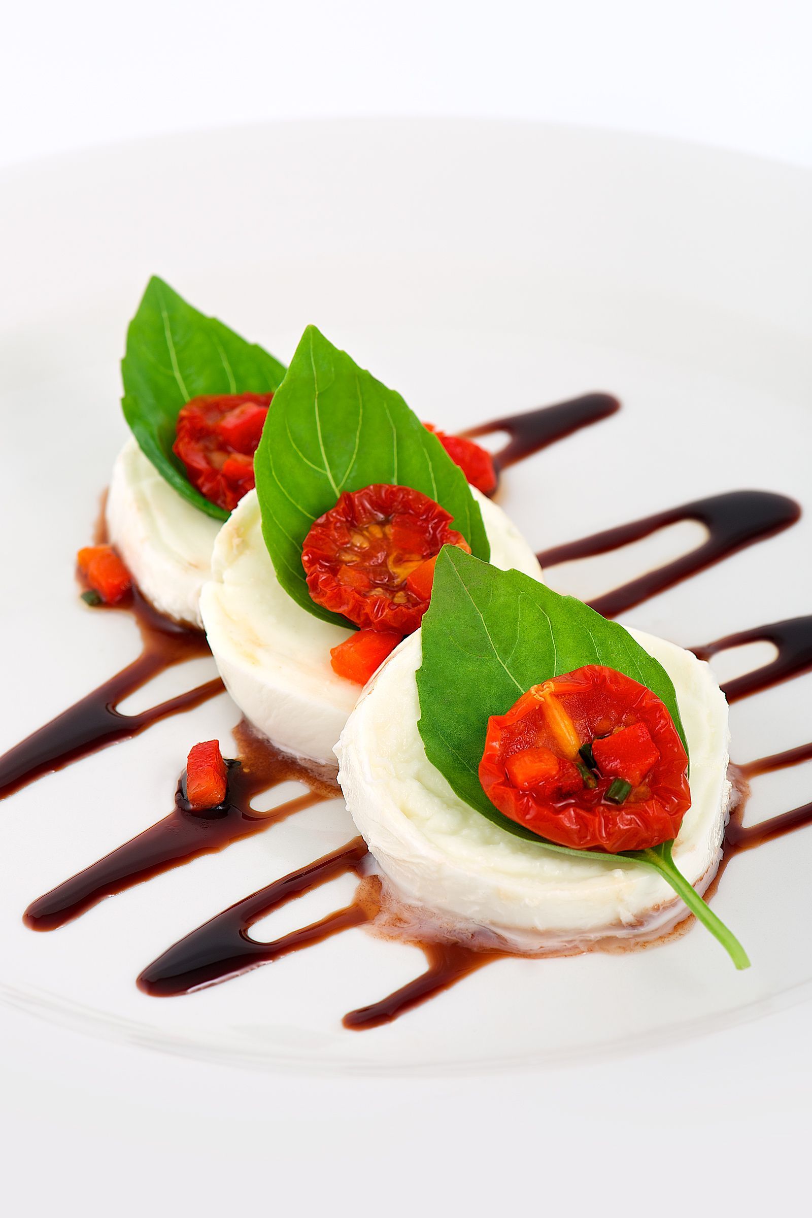 Caprese salad: mozzarella, tomatoes, basil, balsamic glaze on a white plate.
