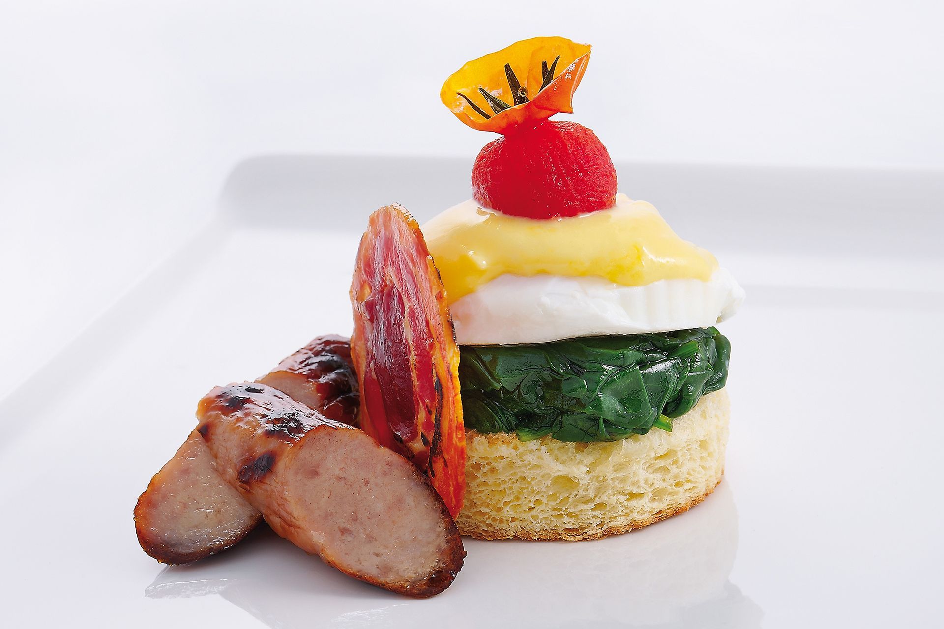 Breakfast dish: sausage, stacked ingredients (English muffin, spinach, egg, hollandaise), garnished with tomato and orange.