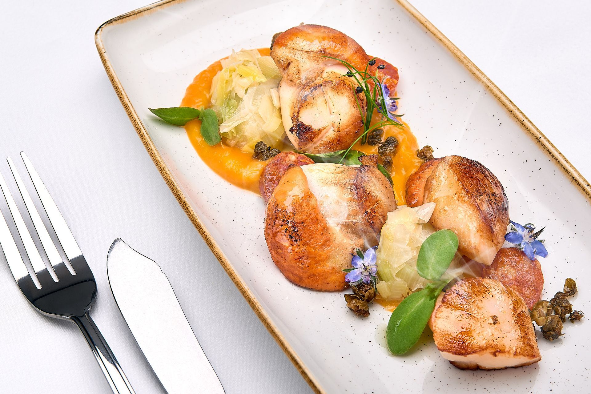 Seared scallops on an oblong plate with butternut squash puree, capers, and garnish.