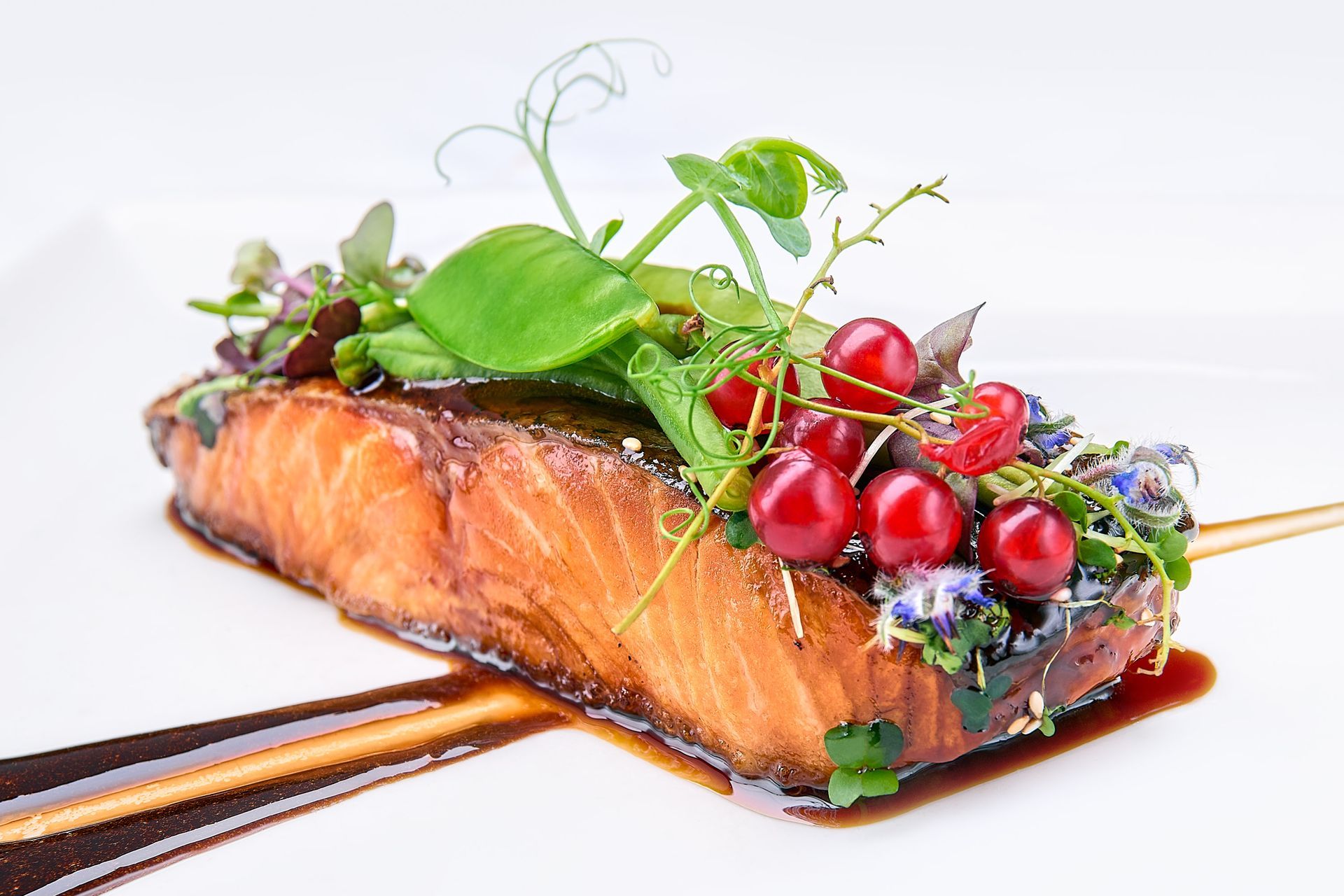 Seared salmon fillet with berry garnish and pea shoots on a white plate, drizzled with sauce.