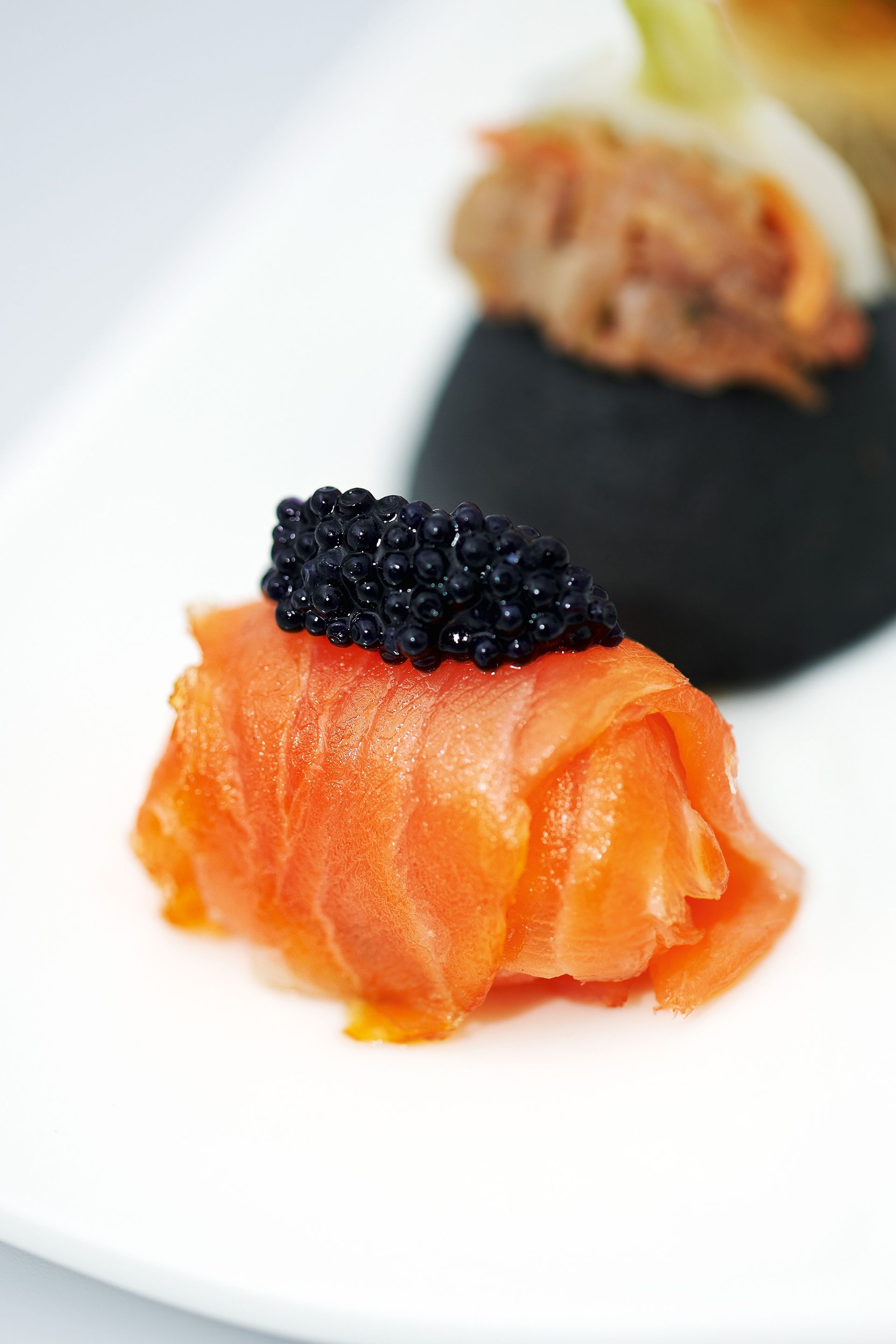 Smoked salmon roll topped with caviar on a white plate.