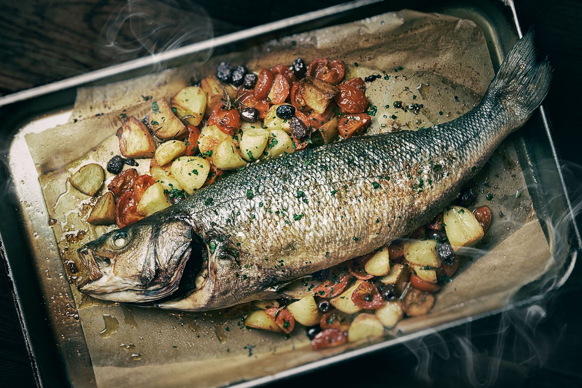 Roasted whole fish with potatoes and tomatoes on a baking sheet.