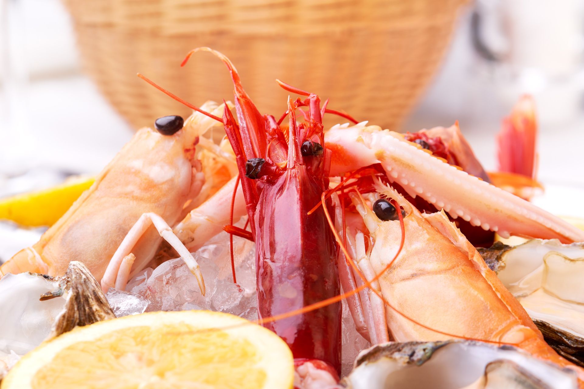 Seafood platter with shrimp, oysters, and lemon slices on ice. Wicker basket in background.