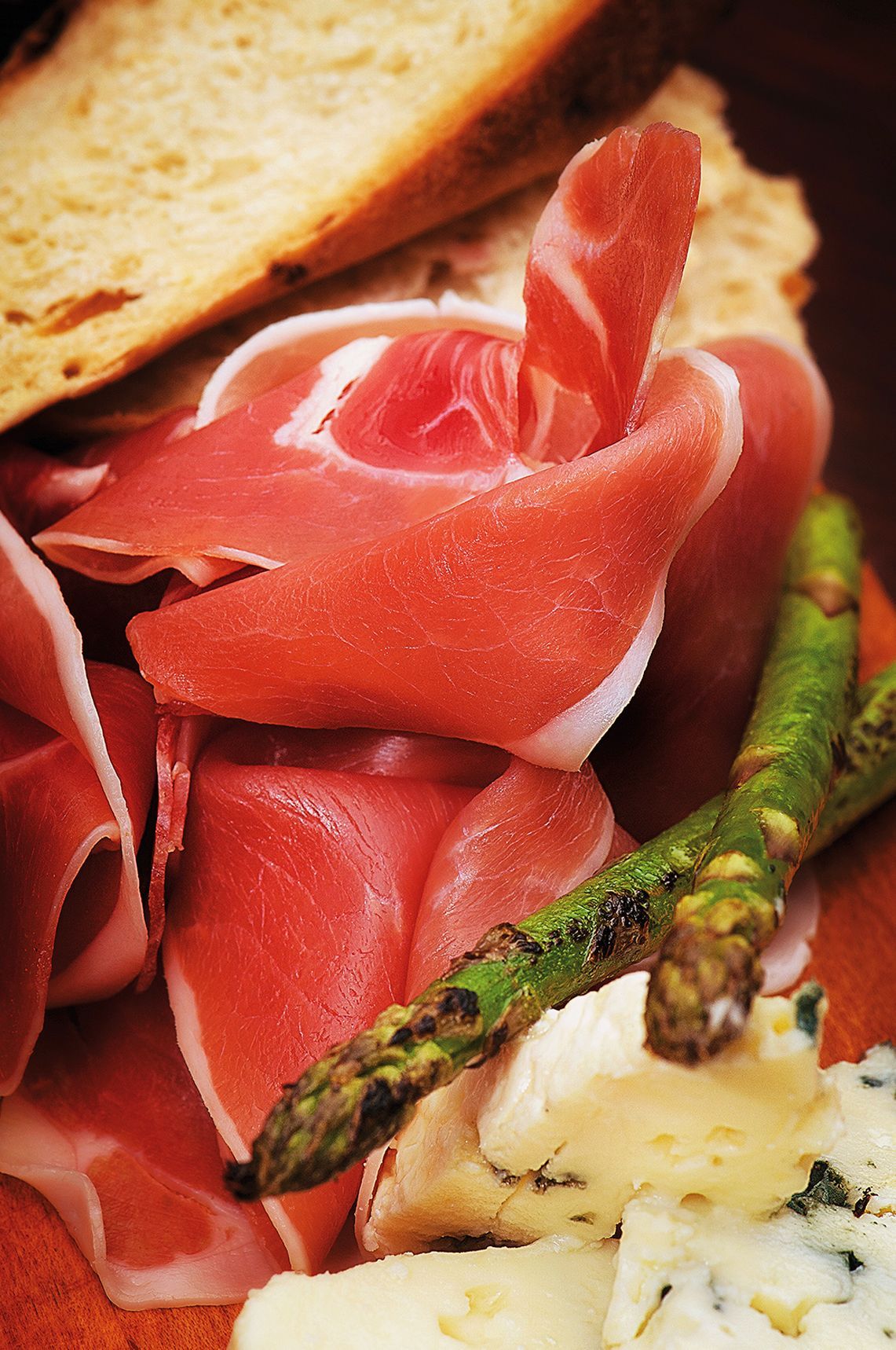 Charcuterie board with prosciutto, asparagus, bread, and cheese.