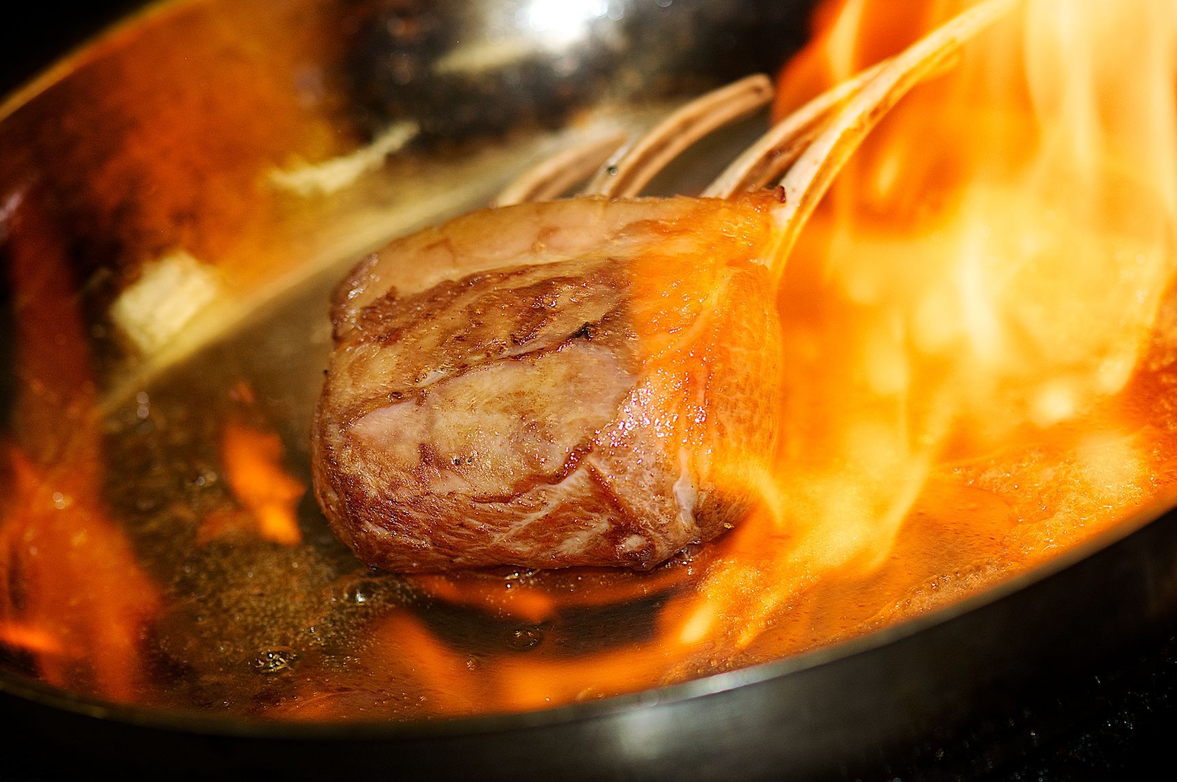 Rack of lamb searing in a flaming pan.