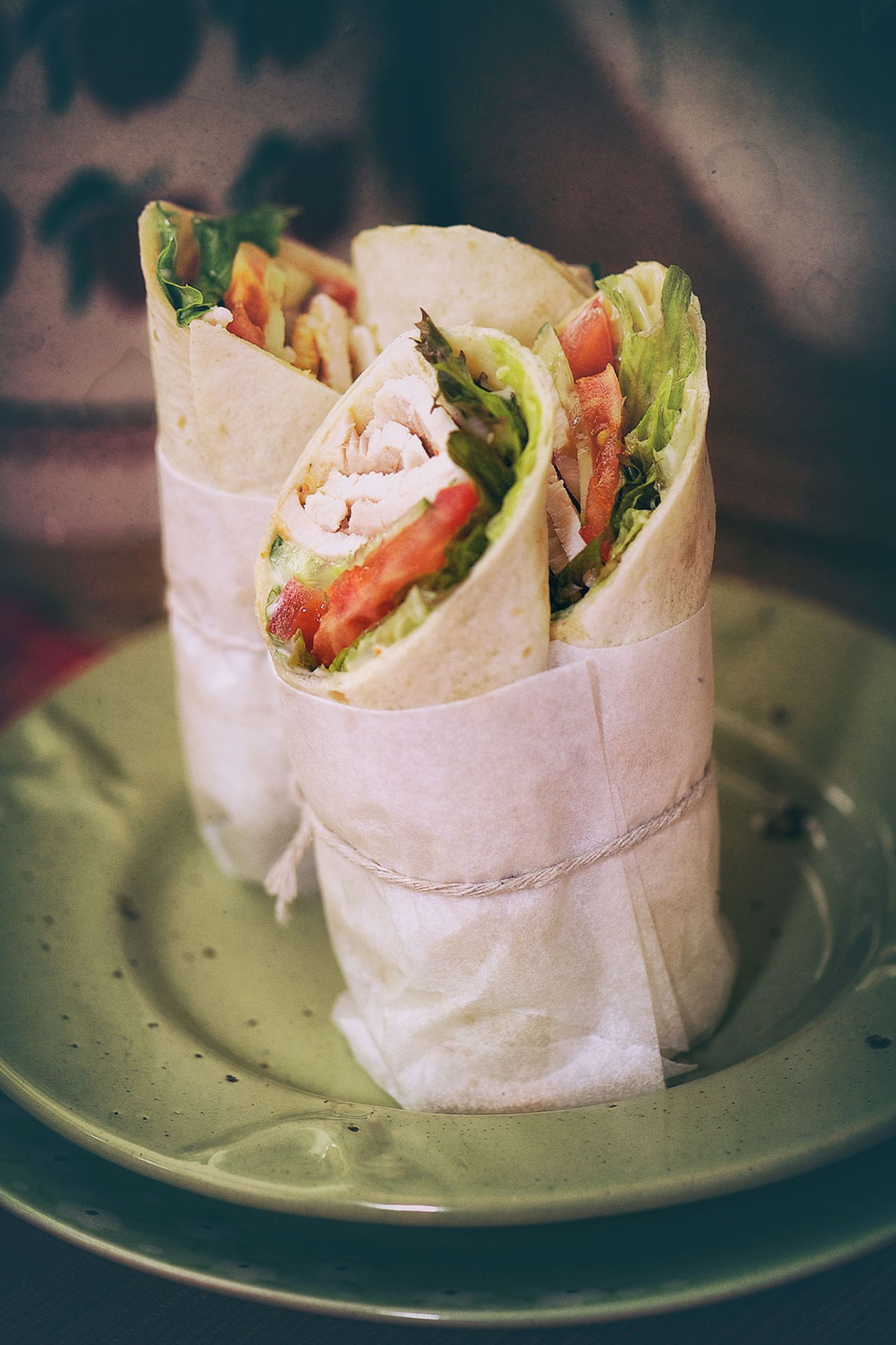 Two chicken wraps wrapped in paper on a green plate.