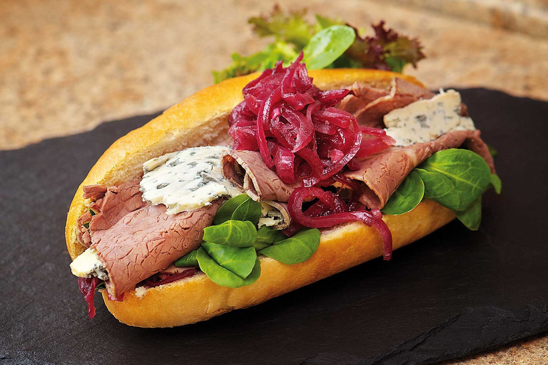 Roast beef sandwich on a bun with blue cheese and pickled onions.