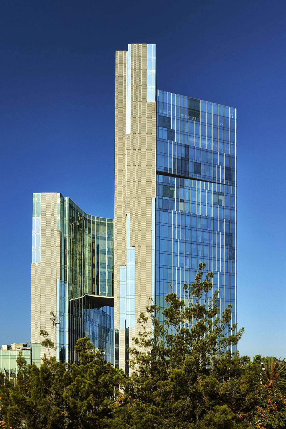 Modern skyscraper with blue glass facade, stone accents, and bright blue sky background.