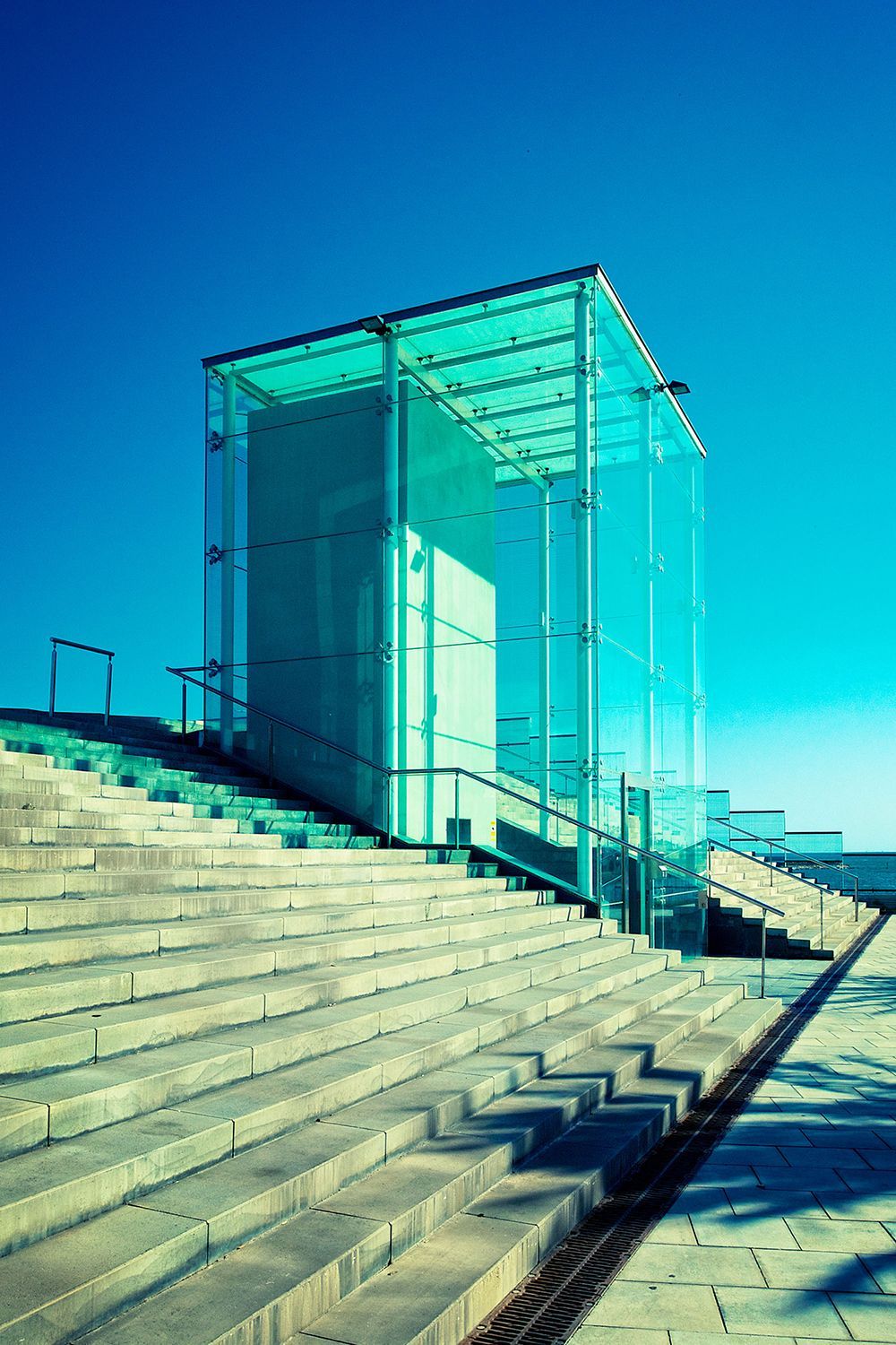 Glass structure atop concrete steps against a clear, blue sky.