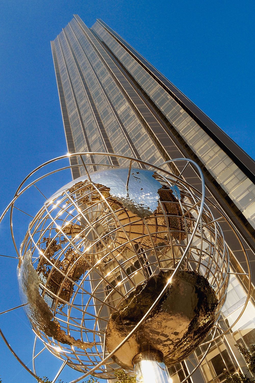 Stainless steel globe sculpture in front of a tall, modern skyscraper against a blue sky.