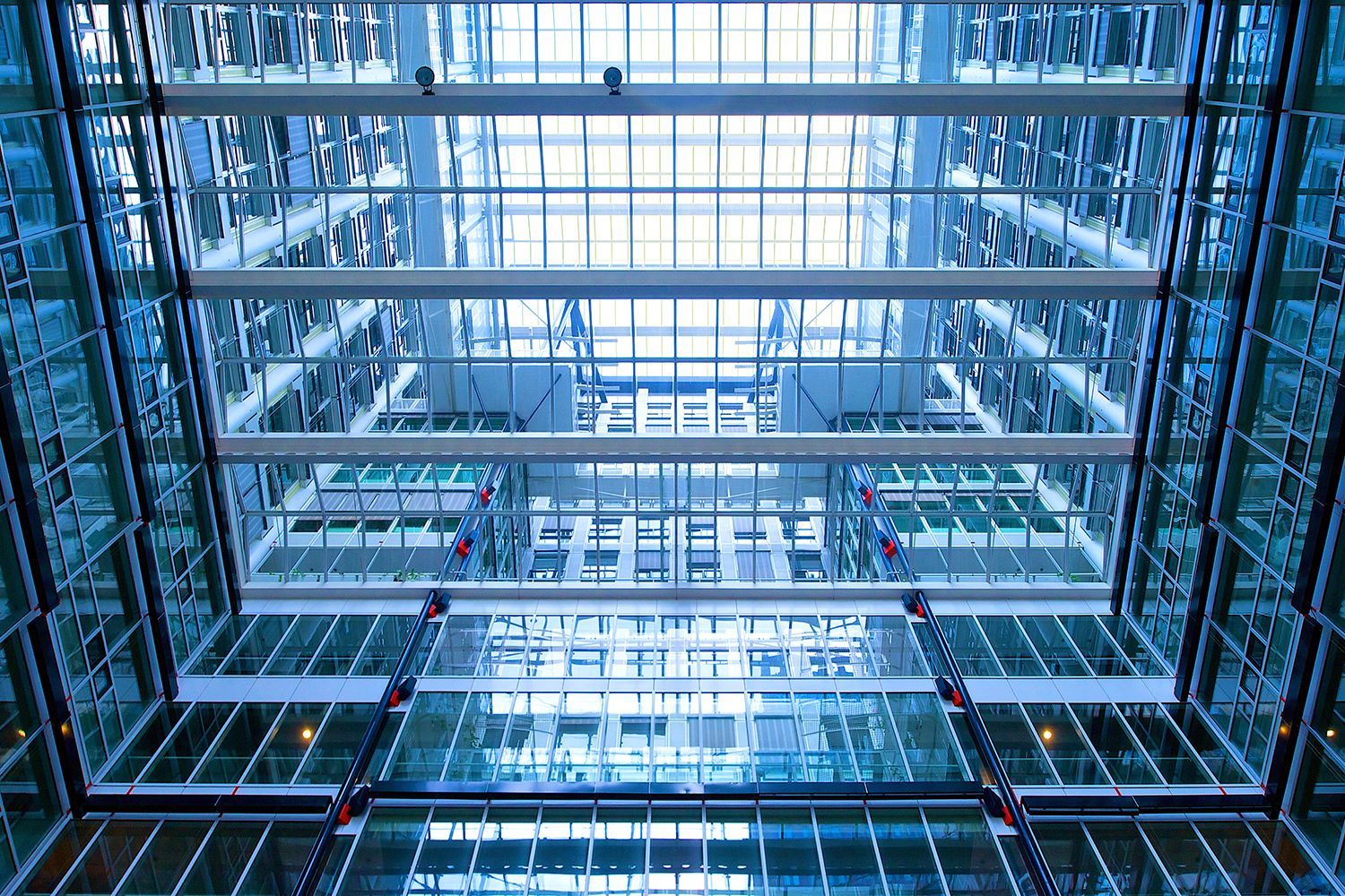Interior view of modern office building with multiple glass-walled floors visible from below, natural light.