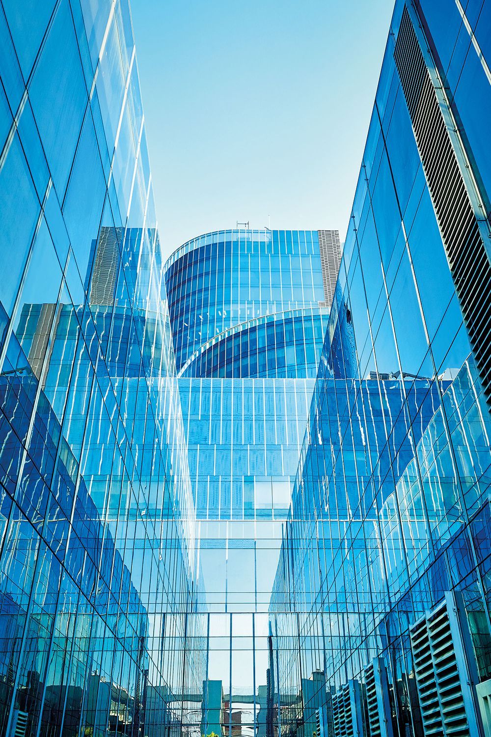 Blue glass skyscrapers against a light blue sky, perspective looking upwards.