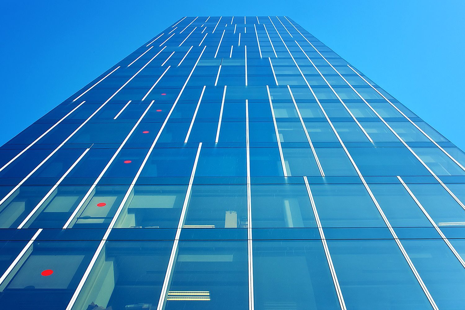 Blue glass skyscraper with white vertical lines against a clear, blue sky.