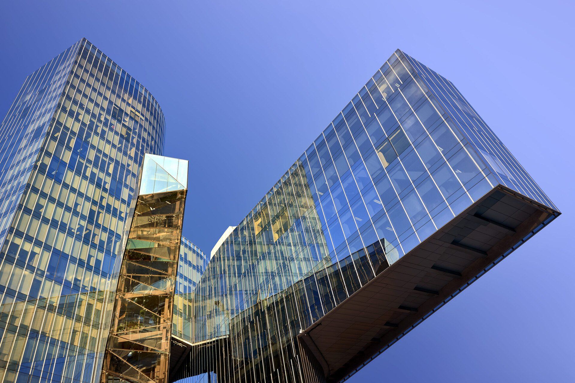 Modern glass skyscrapers connected by bridges against a clear blue sky.