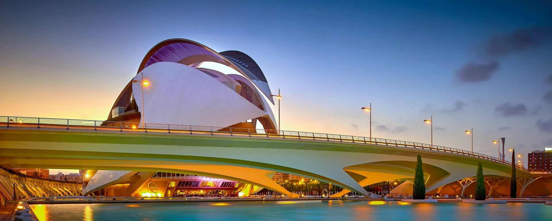 Modern architecture overlooking a body of water at dusk. Structures in white, purple, and yellow.