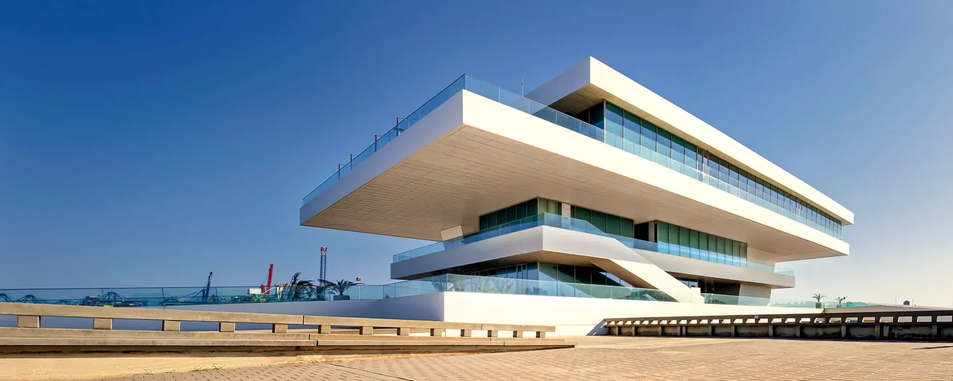 Modern angular building with stacked cantilevered terraces against a clear blue sky.