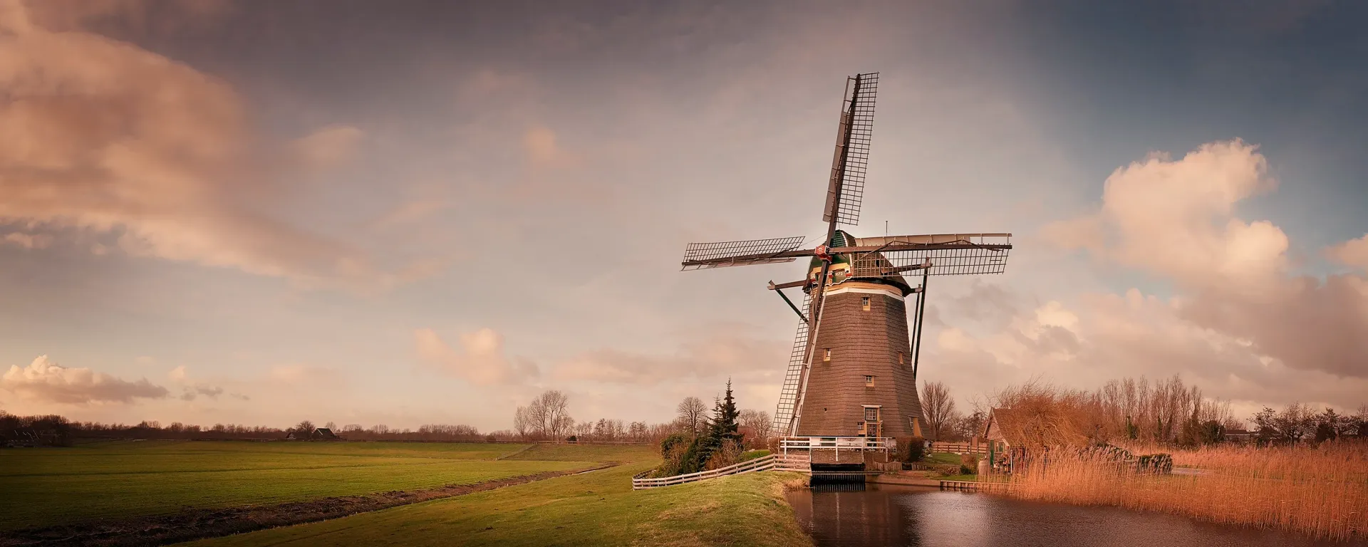 Windmill in a field with a cloudy sky and a body of water.