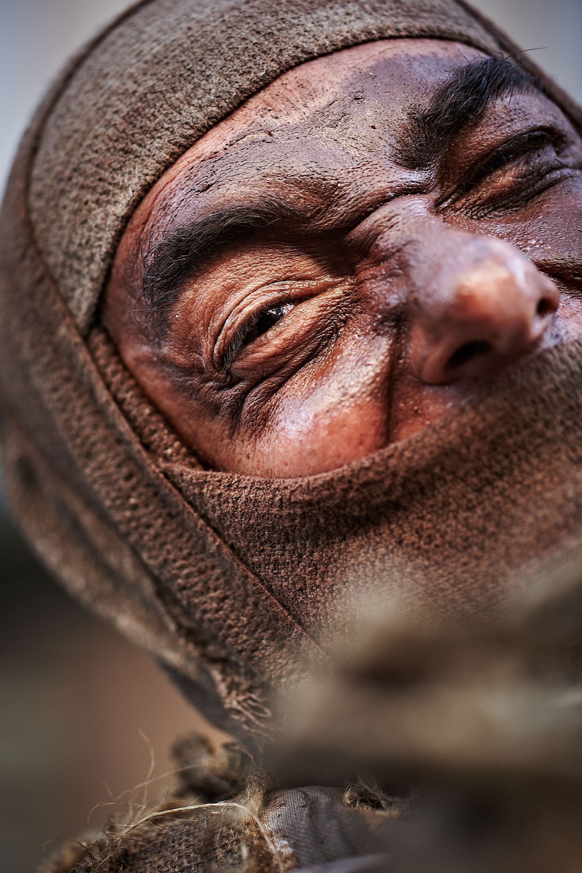 Close-up of a person's face, covered in dirt and a brown head covering, with an intense expression.
