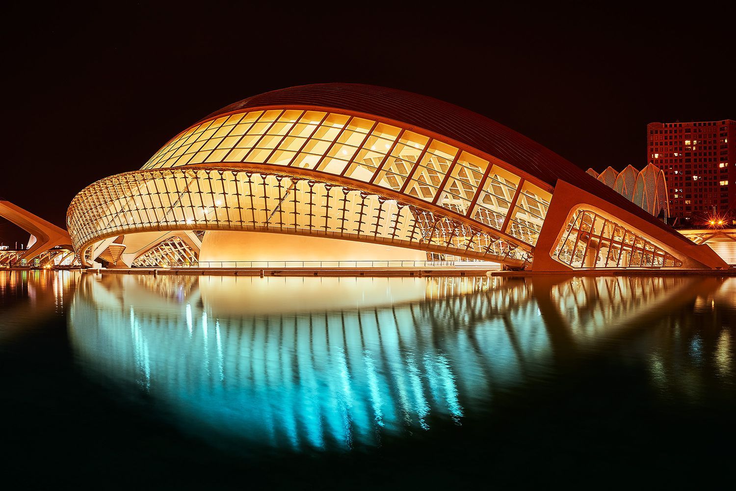 Illuminated, modern building reflecting in water at night. Glass and steel structure. Valencia, Spain.