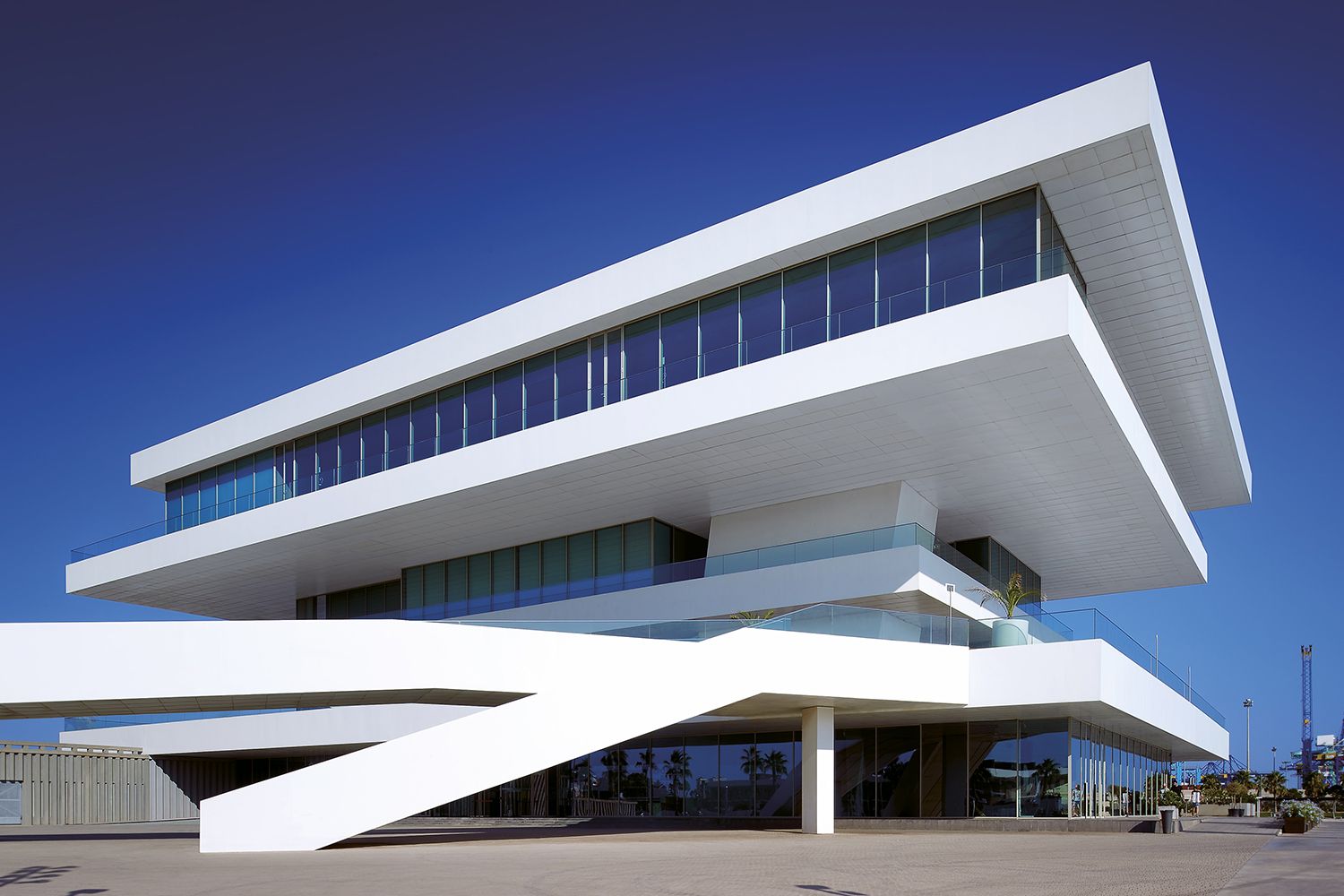 Modern white building with angular design and large windows against a blue sky.