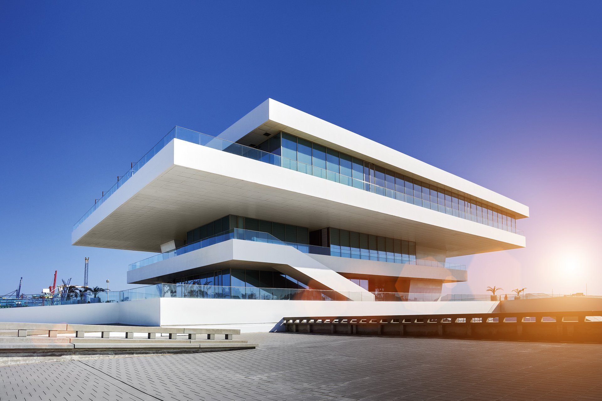 Modern white building with layered design and glass windows against a bright blue sky.