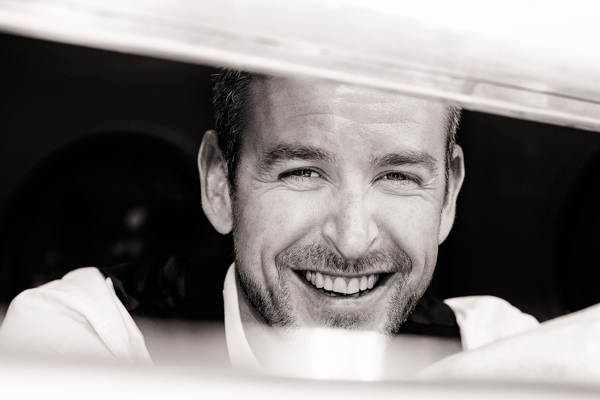 Man smiling, peering through a window. Black and white photograph.