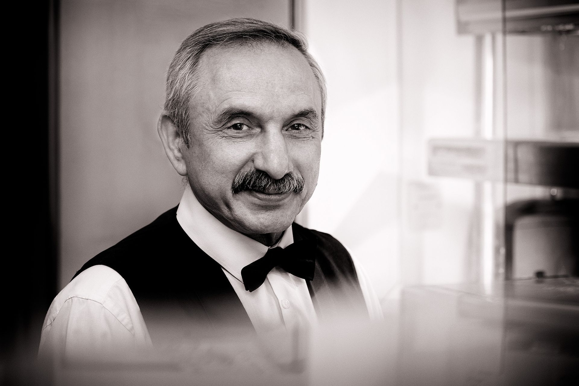 Man with mustache and bow tie smiles, wearing a vest and collared shirt.