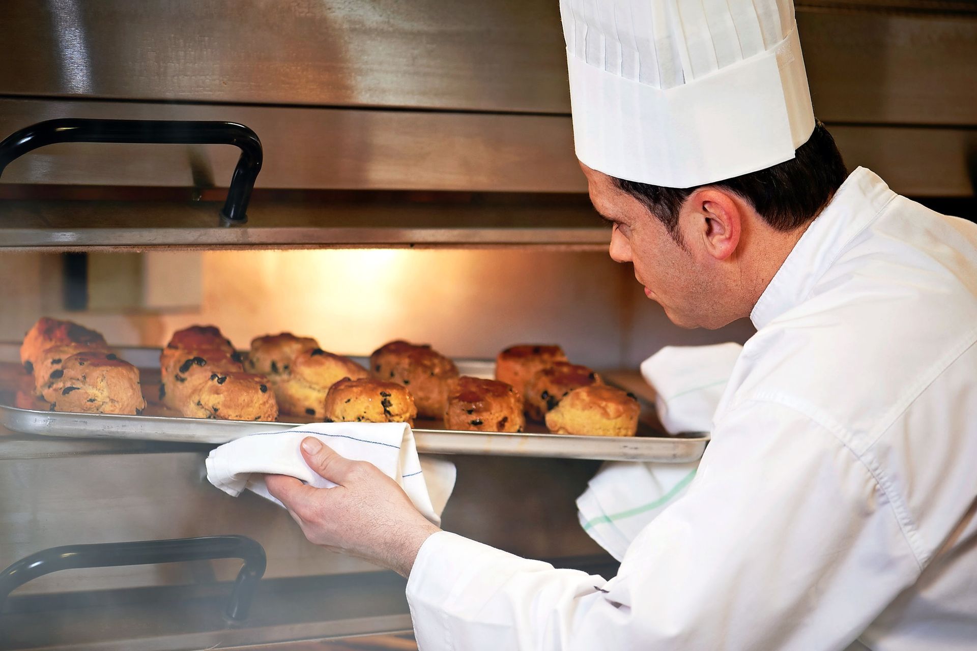 Chef removing a tray of baked goods from a hot oven.