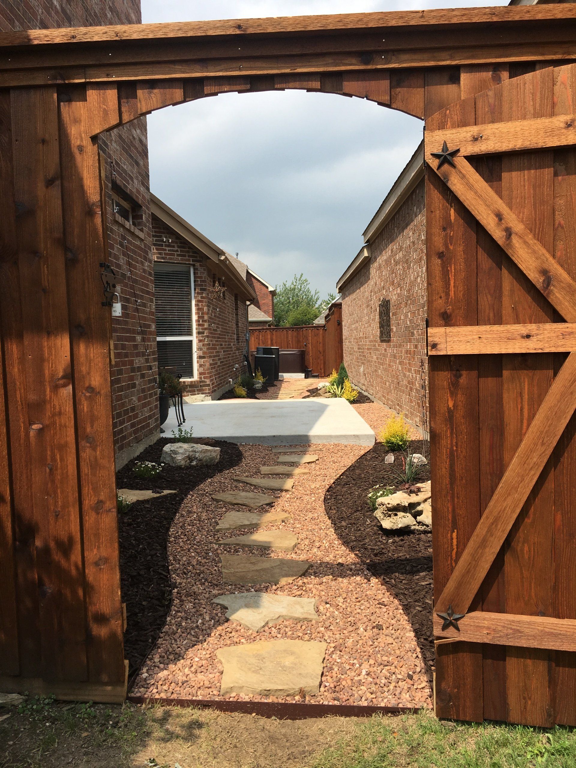 Fence with a paved walkway and rocks leading into a backyard
