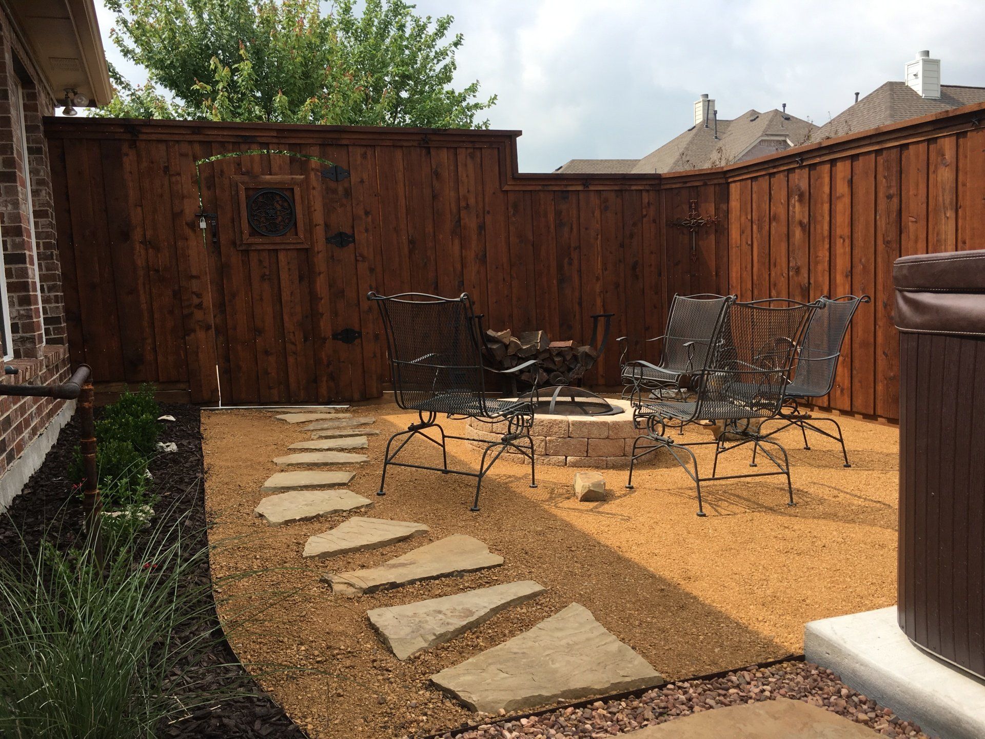 Paved walkway leading past a packyard with pebbles and chairs and a firepit