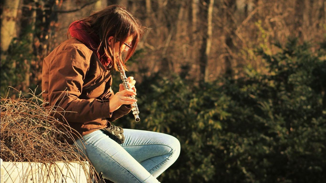A woman is sitting on a bench playing a flute.