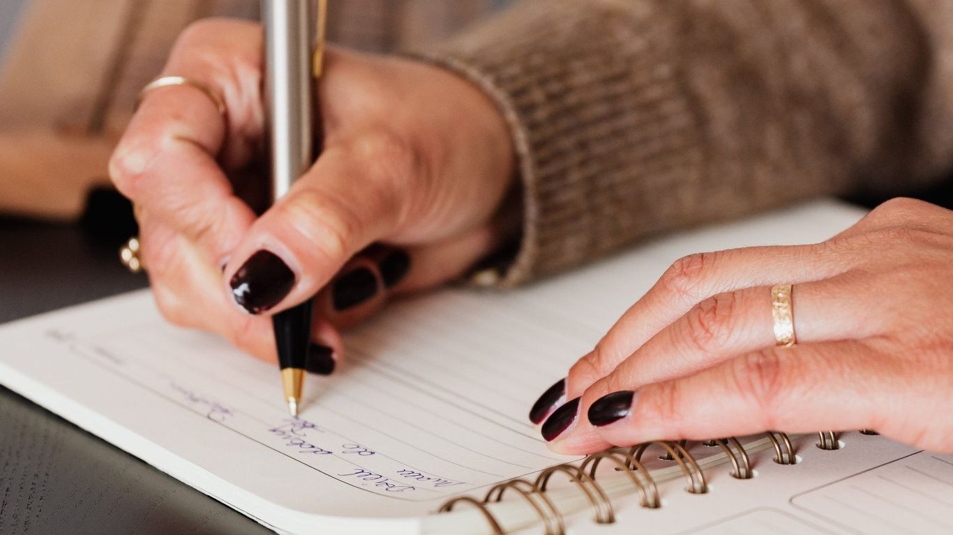 A woman is writing in a notebook with a pen.
