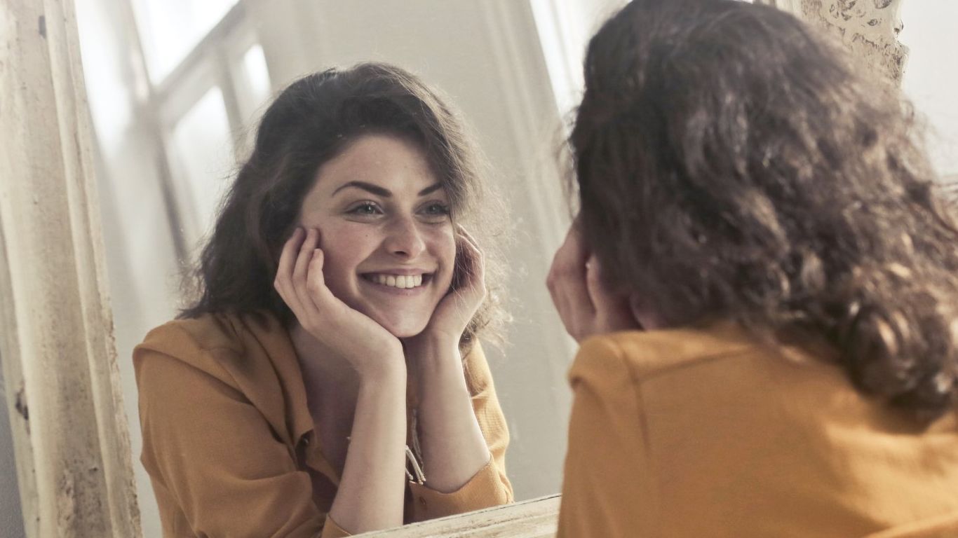 A woman is smiling while looking at herself in a mirror.