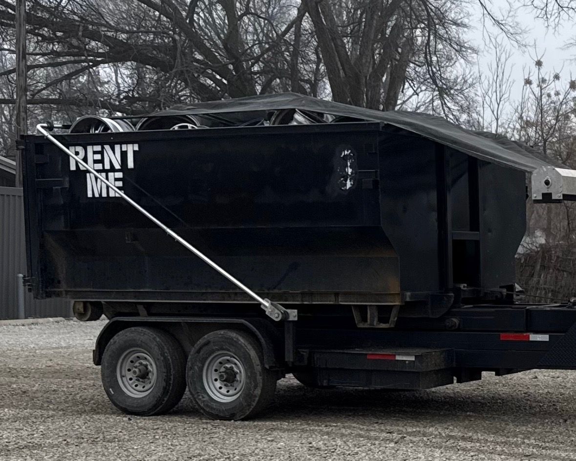 A large black dumpster is sitting on top of a dirt road.