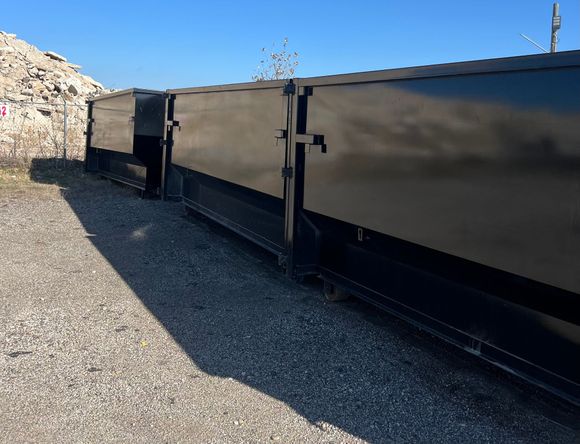 A large black dumpster is sitting on top of a dirt road.