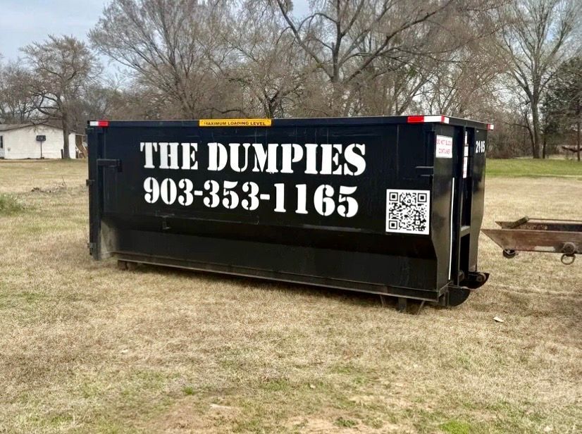 A large black dumpster is sitting on top of a dirt road.
