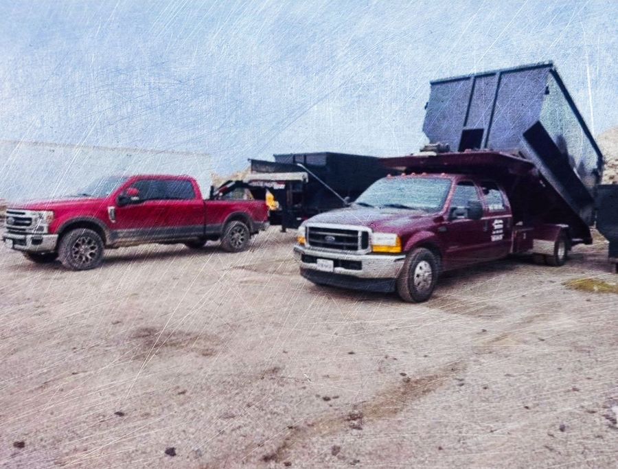 A large black dumpster is sitting on top of a dirt road.