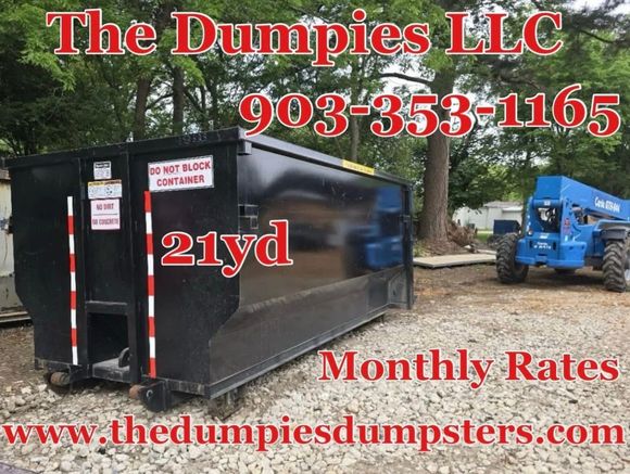 A large black dumpster is sitting on top of a dirt road.