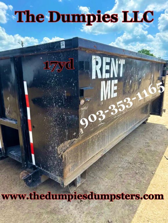 A large black dumpster is sitting on top of a dirt road.