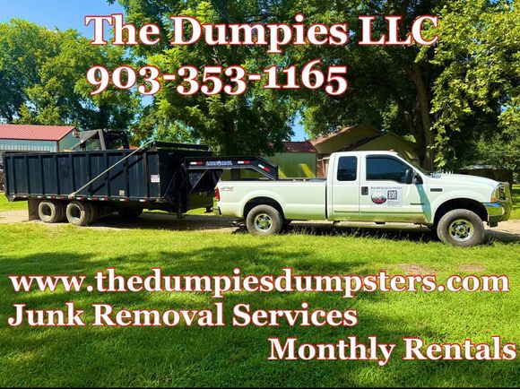 A large black dumpster is sitting on top of a dirt road.