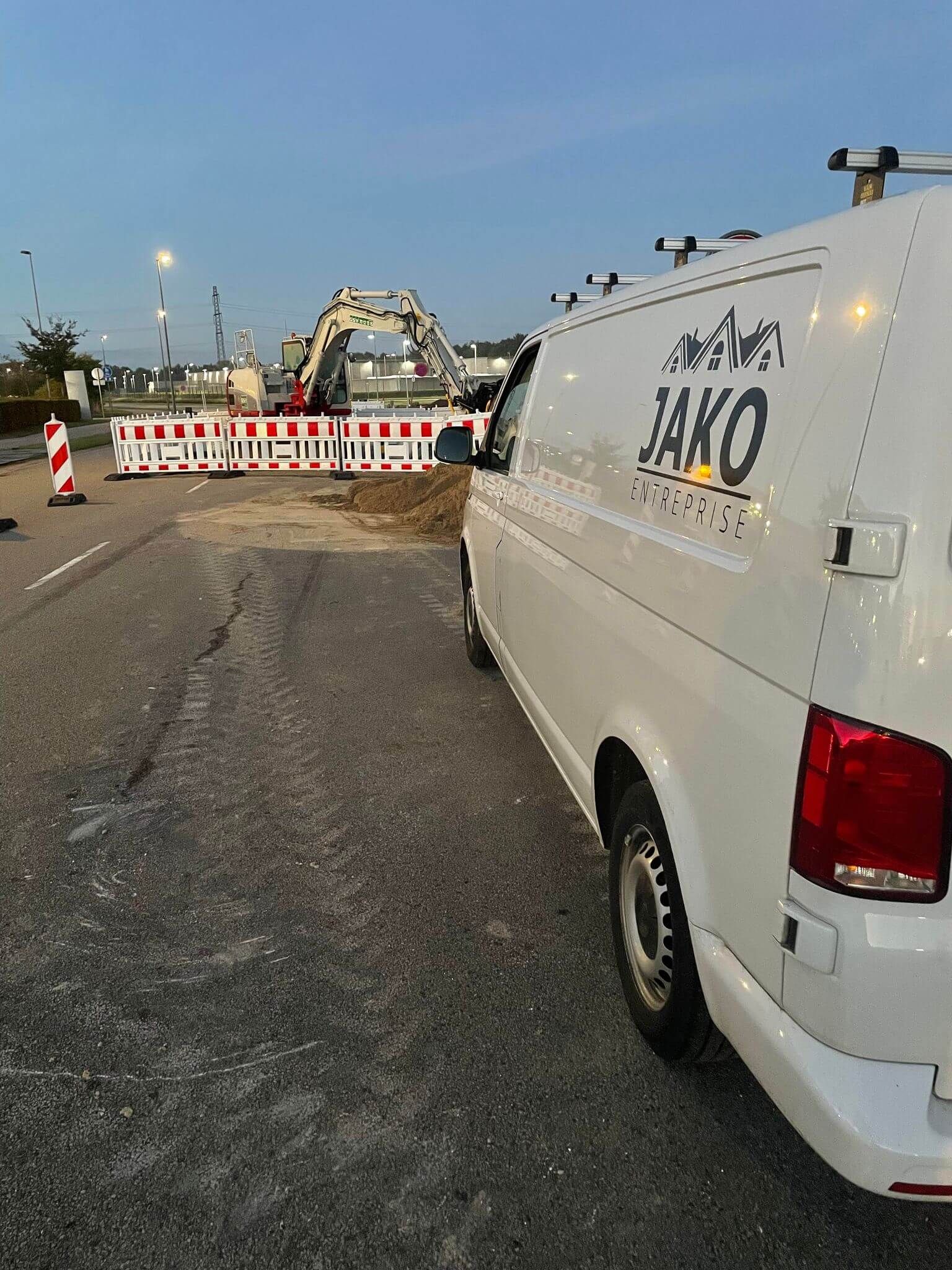 En hvid varevogn med ordet jako på siden er parkeret i siden af vejen.