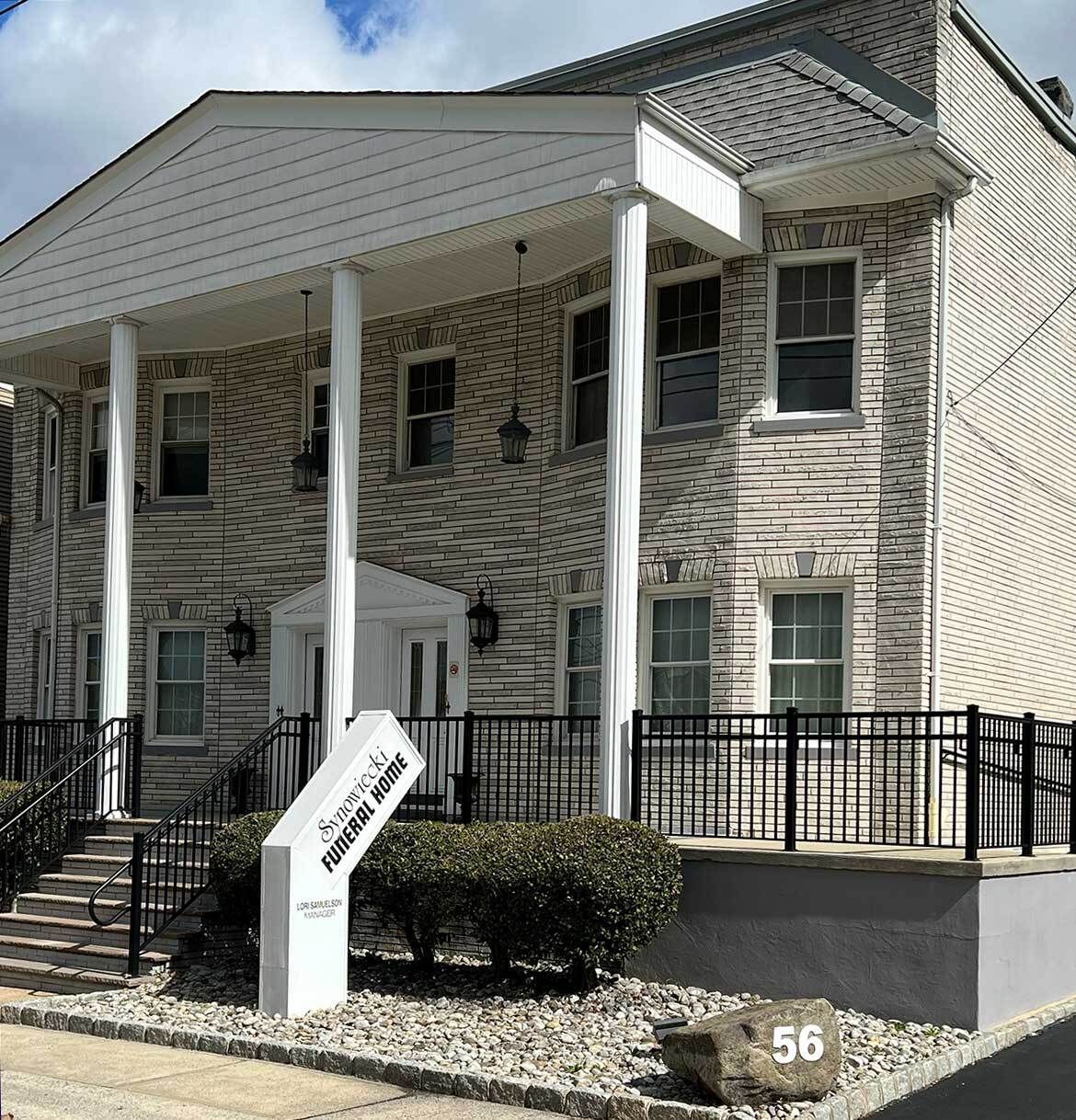 Two-story building with a white porch and pillars. A sign reads 