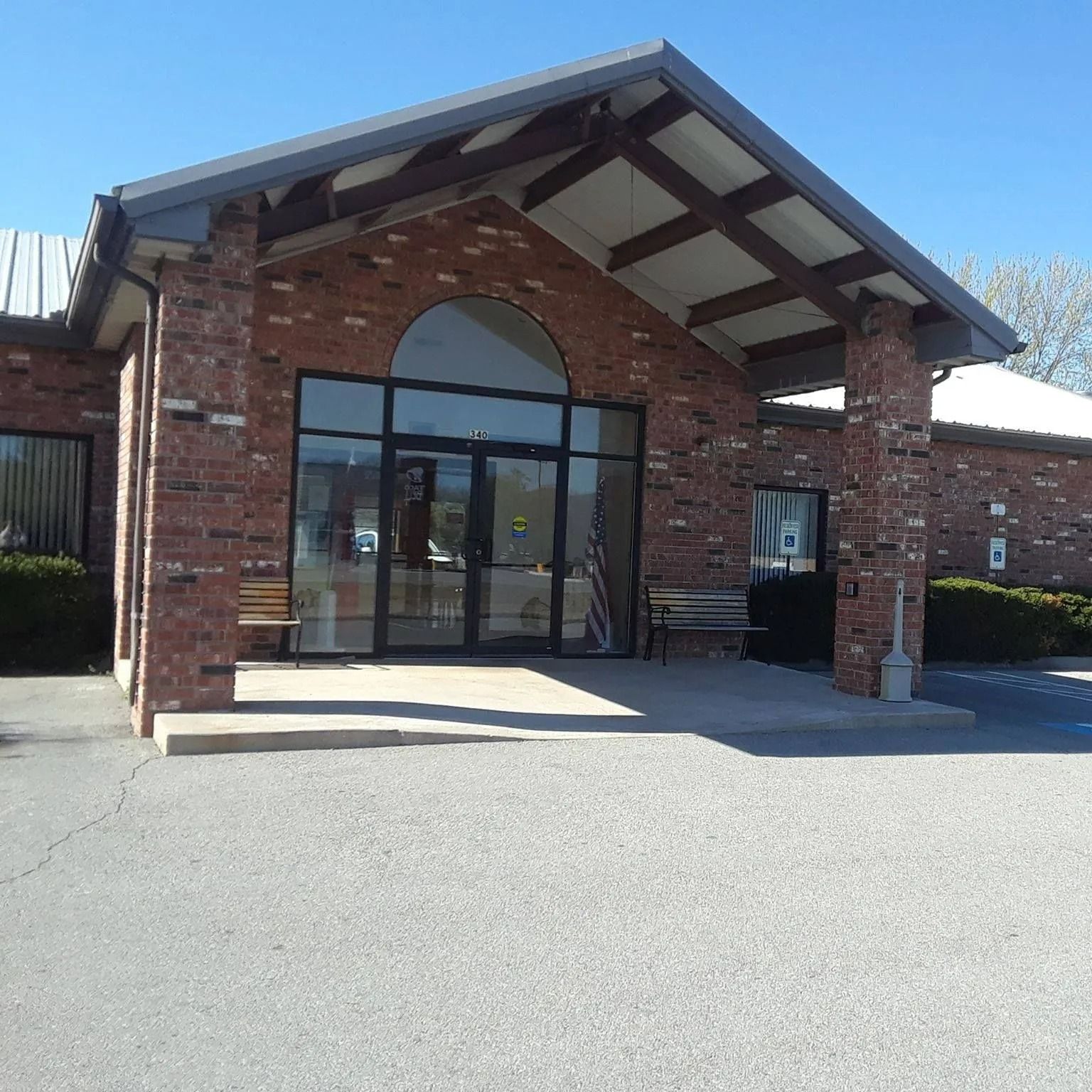 Brick building entrance with glass doors, benches, and overhang; blue sky.