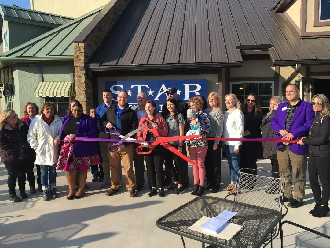 Group cuts ribbon in front of Star Estate building. People smiling, some holding scissors, in daylight.