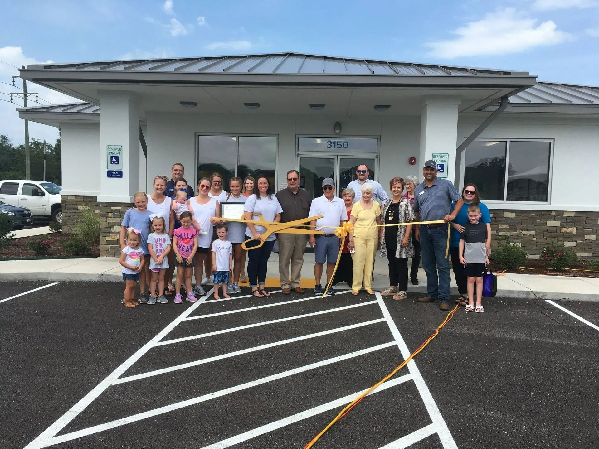 People cutting ribbon in front of a new building; sunny day.