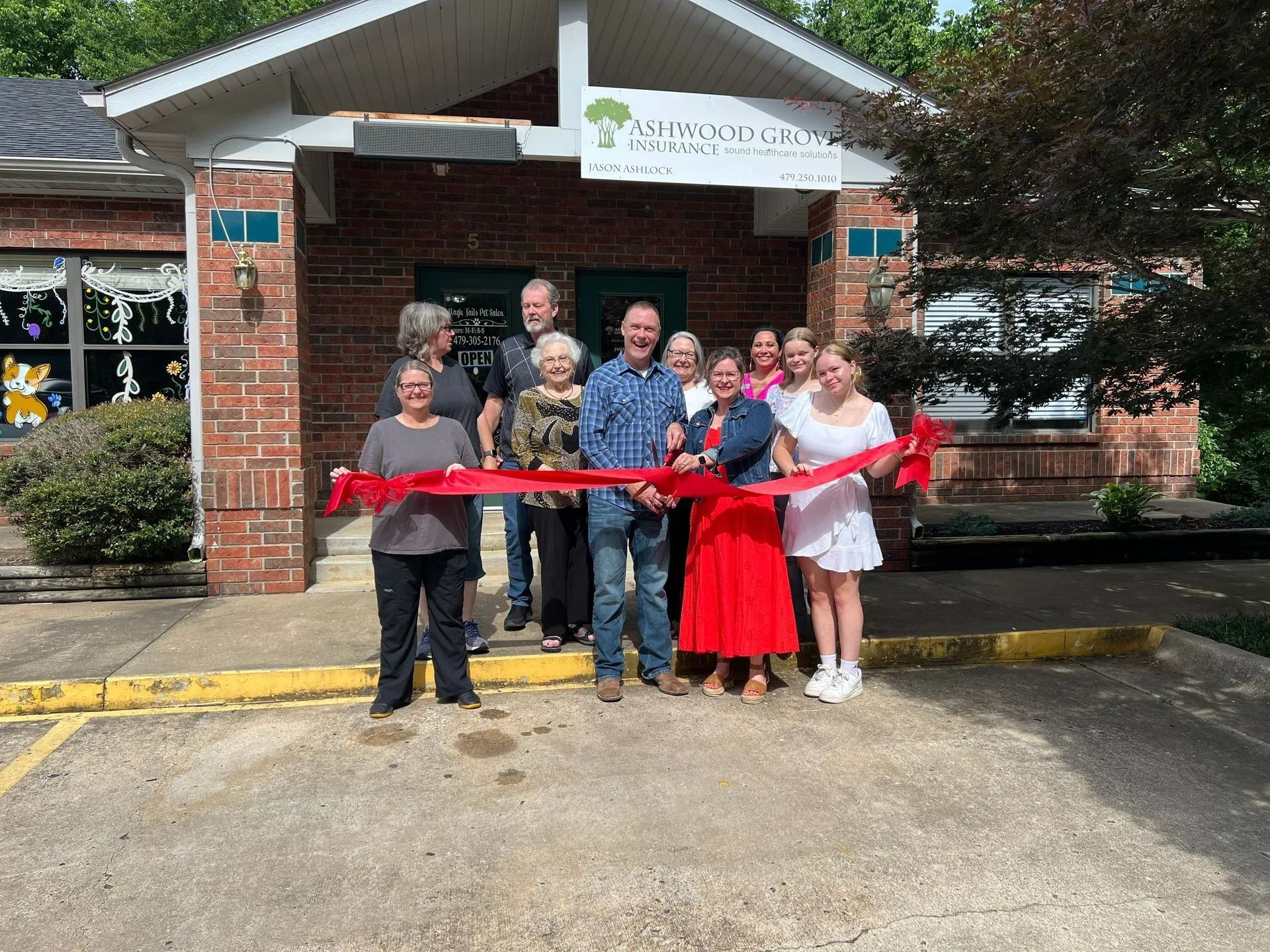 People cutting a red ribbon at the entrance of a brick building, likely a business.