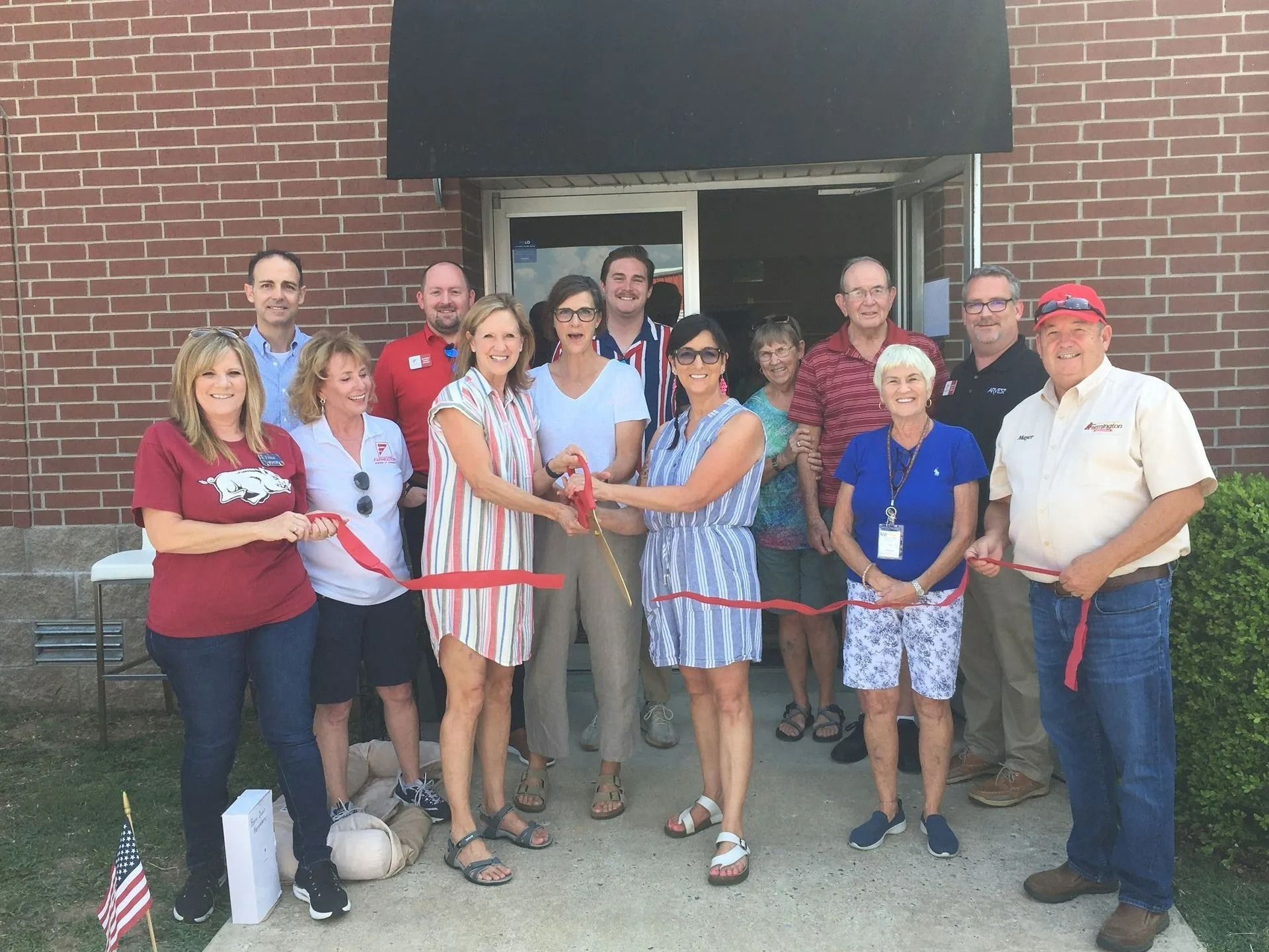 Group cuts red ribbon in front of brick building; grand opening.